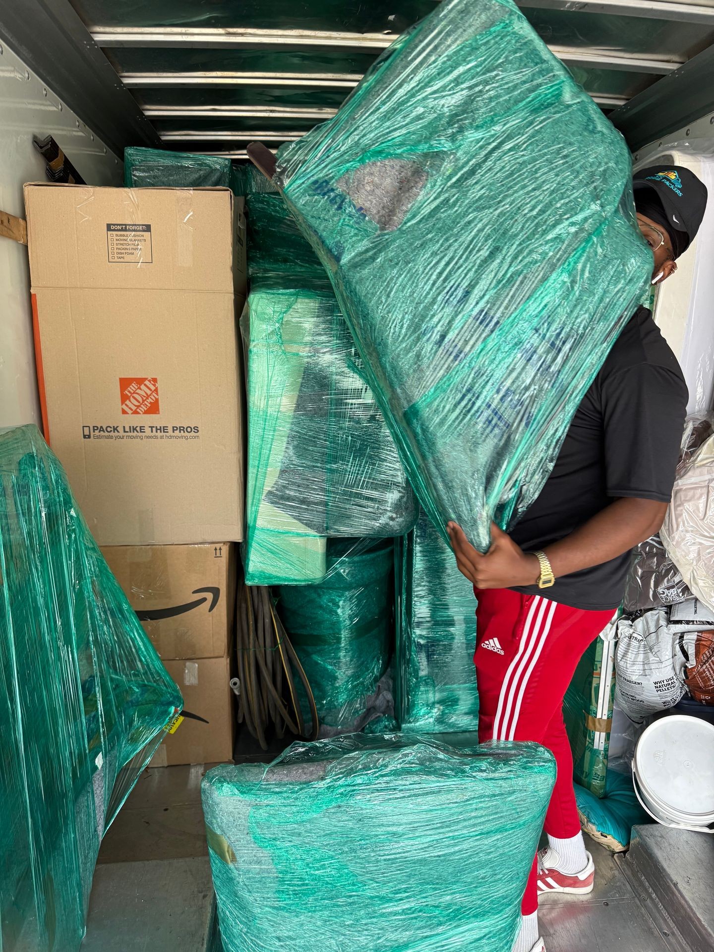 Person in red pants organizing wrapped furniture and boxes inside a moving truck.