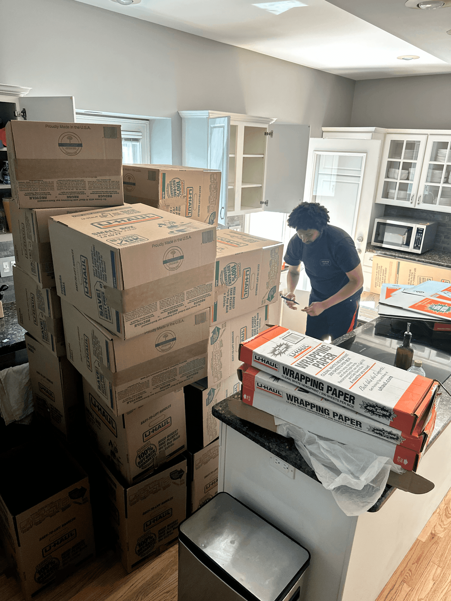 Person packing boxes in a kitchen with stacks of U-Haul moving boxes and wrapping paper.